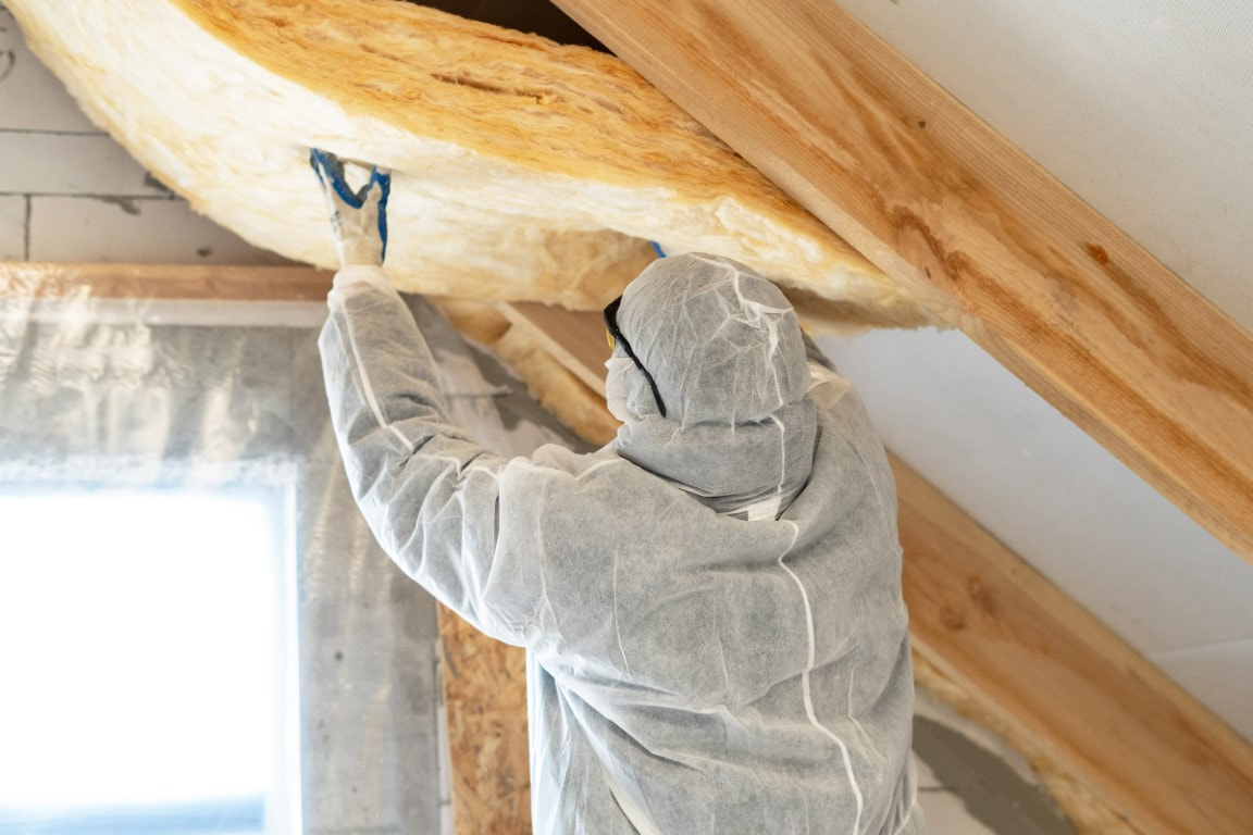 A picture of a person in a white suit and goggles working on a roof insulation