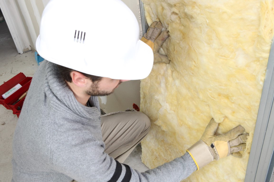 A picture of a man wearing a hard hat and gloves placing an insulation material