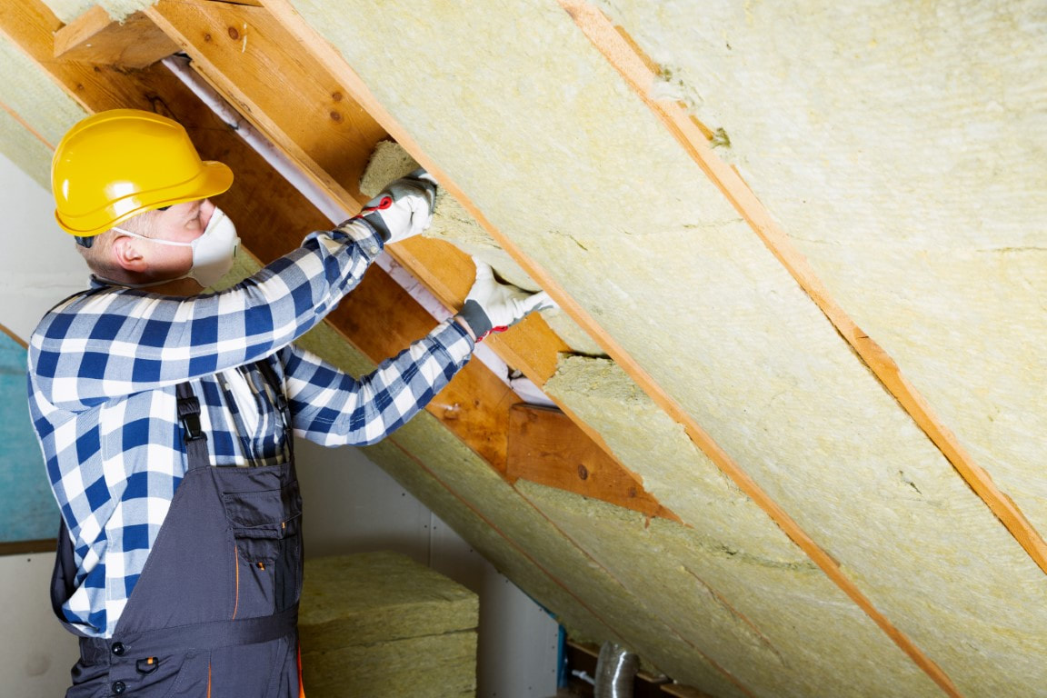 A picture of a man wearing a helmet and gloves putting insulation material in the attic