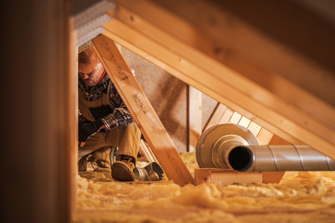 A picture of a man fixing insulation at the attic of the house