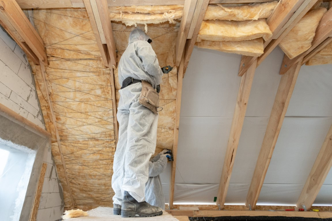 A picture of a person standing at the house fixing insulation in the ceiling
