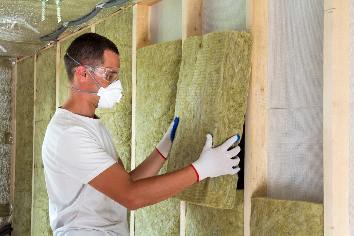 A picture of a man equipped with  safety goggles and a white mask placing a piece an insulation material 
